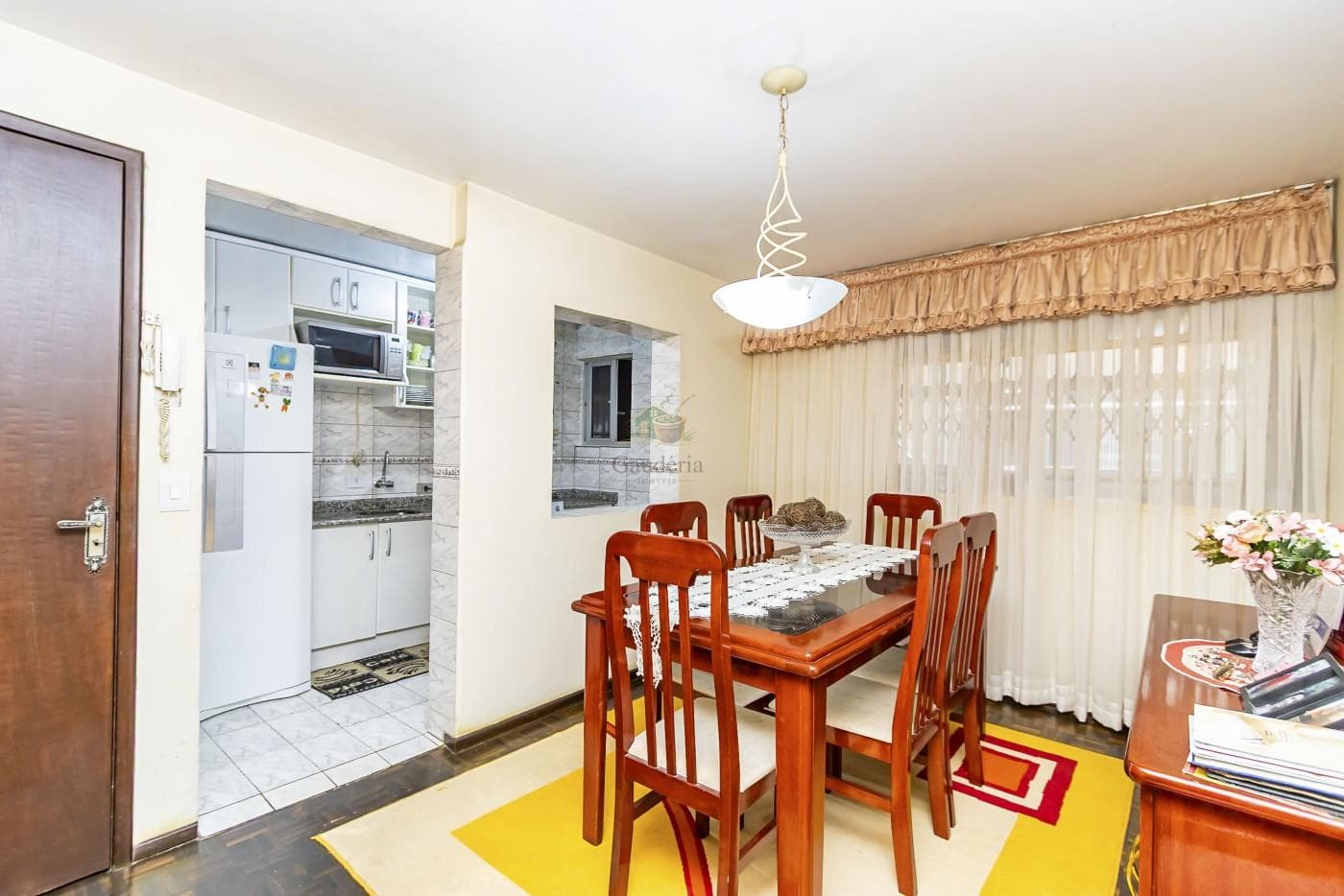 Sala de jantar com mesa de madeira, seis cadeiras e passagem para a cozinha.