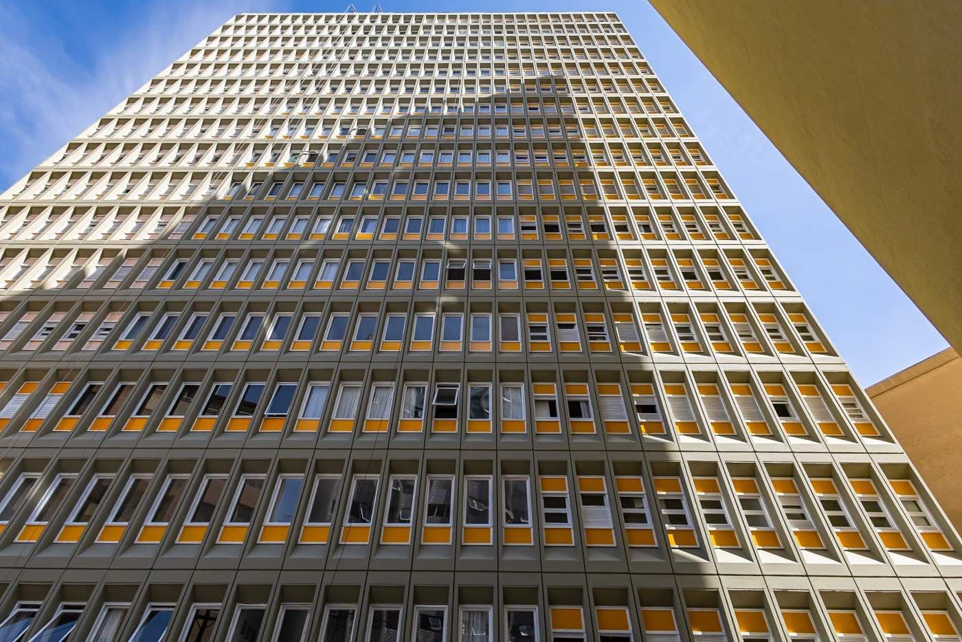 Fachada de edifício alto com diversas janelas e detalhes em amarelo.
