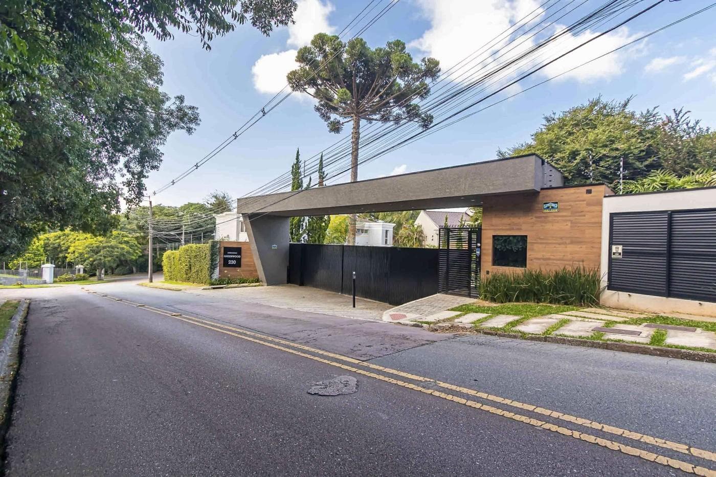 Fachada do condomínio com portaria moderna, portão preto e arborização.